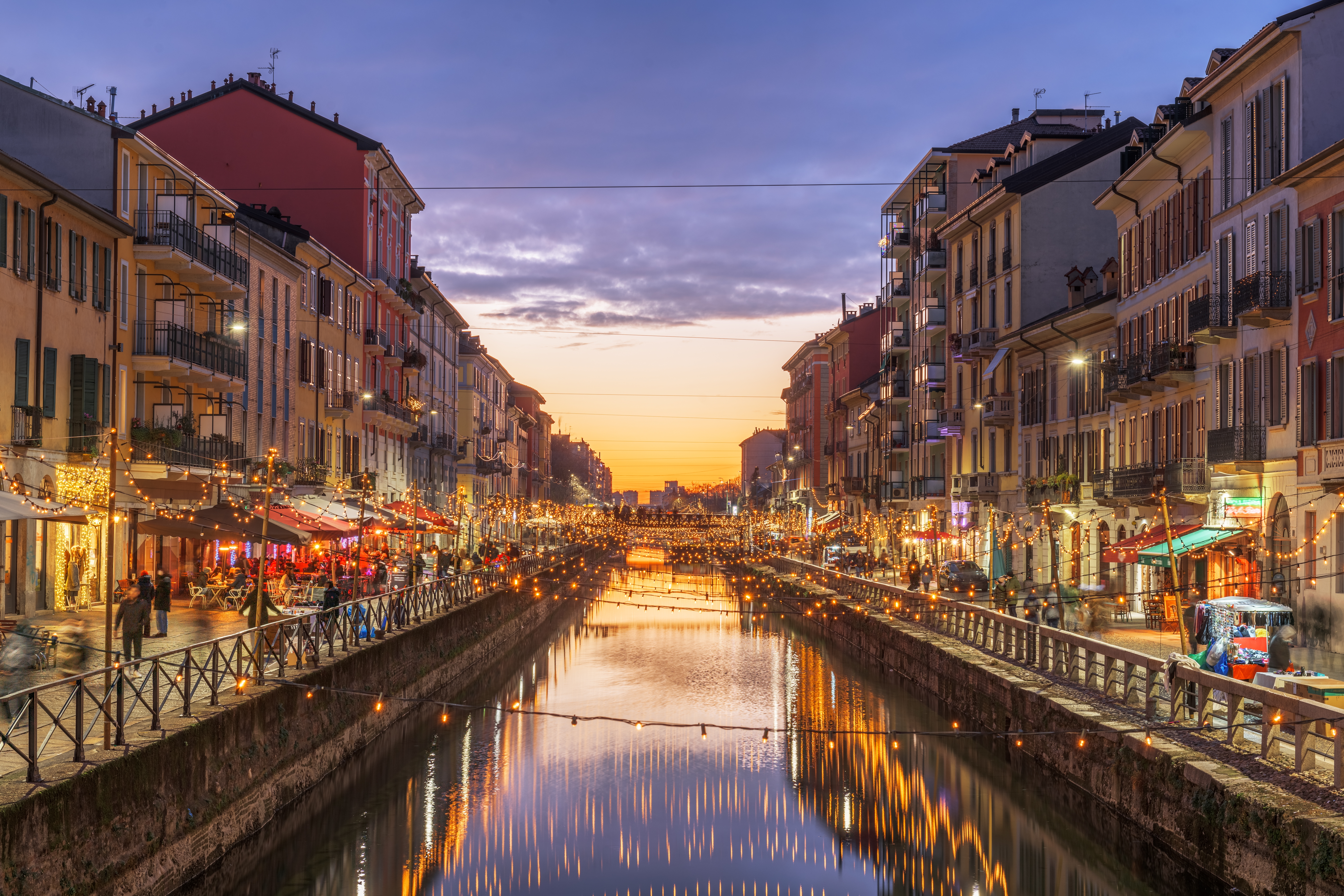 Historic Italian city street with vintage buildings and cozy lights reflecting on a central river at dusk.