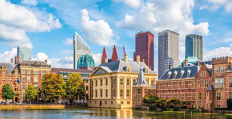 A scenic view of The Hague, Netherlands, showing a mix of historic buildings and modern skyscrapers along the Hofvijver lake