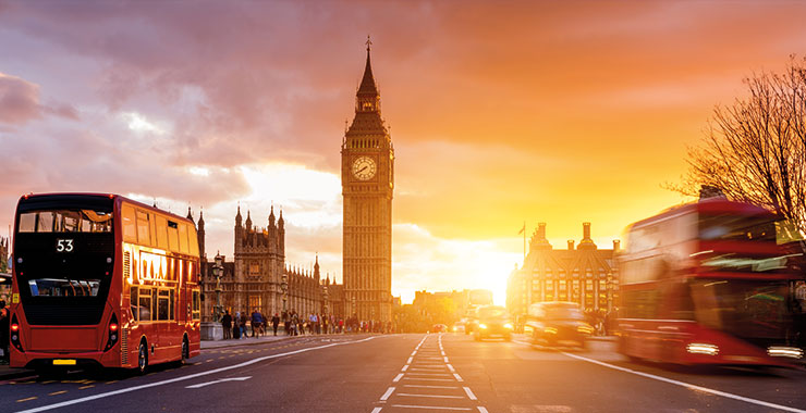 Sunset view of Big Ben and the Houses of Parliament in London, with red double-decker buses passing by