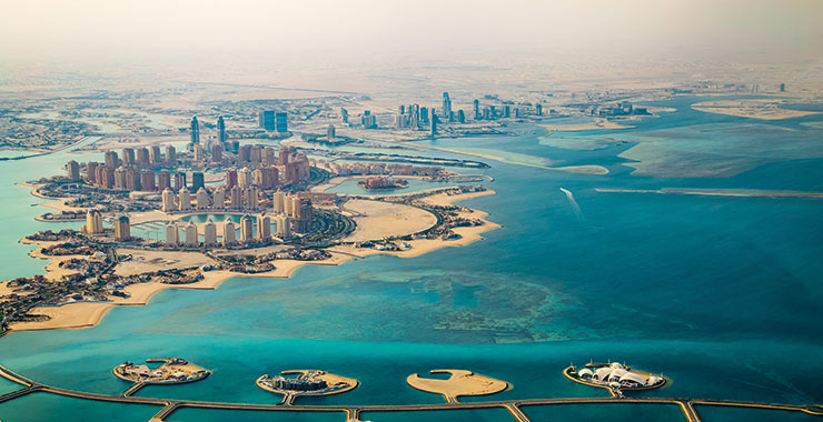 An aerial view of Doha, Qatar, showcasing the city's modern skyline, artificial islands, and the Arabian Gulf