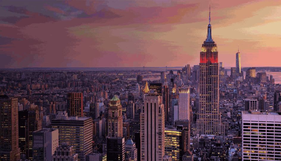 A panoramic view of New York City at sunset, featuring the iconic Empire State Building towering above the skyline