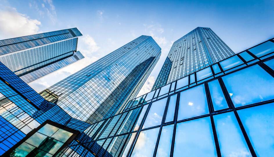 A cluster of modern, glass-fronted skyscrapers reaching towards a bright blue sky with white clouds