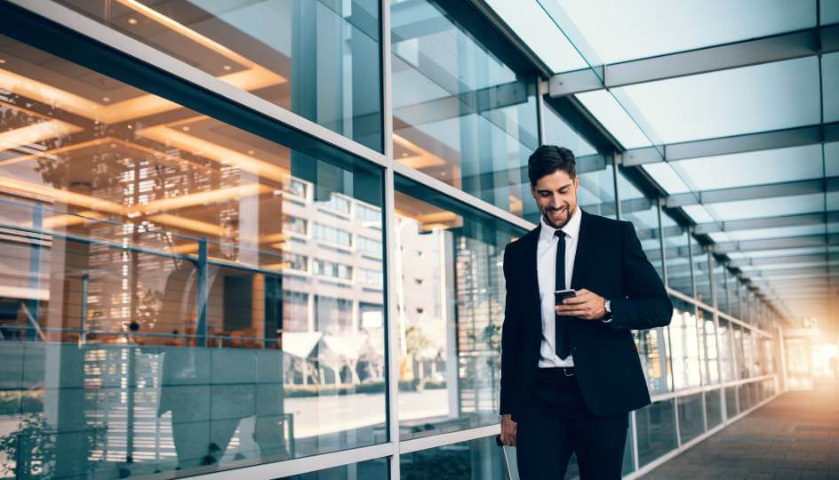 Happy young businessman walking and looking at mobile phone at airport