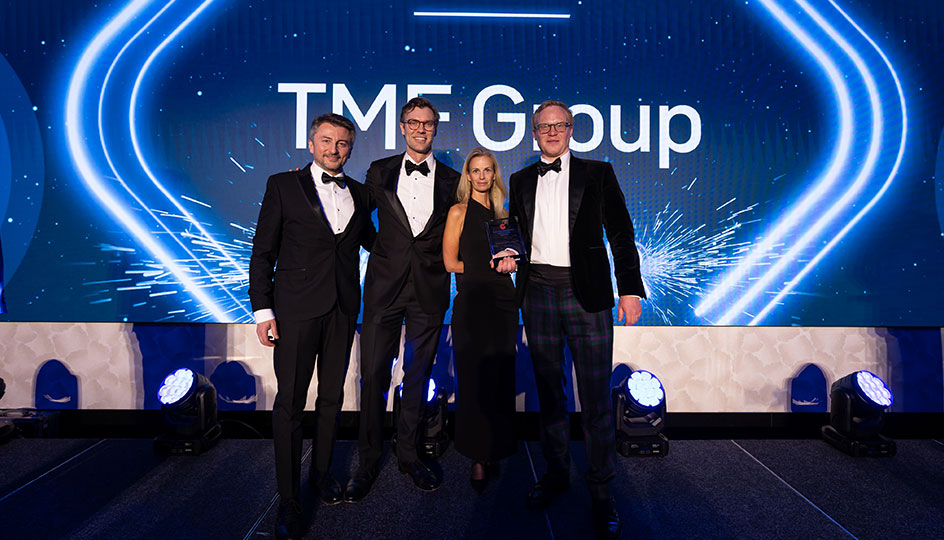 Four people in formal attire stand on stage holding an award, with the illuminated 'TMF Group' logo displayed on the screen behind them