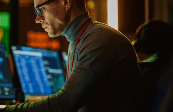 A man in a sweater focused on his computer, engaged in work at a desk